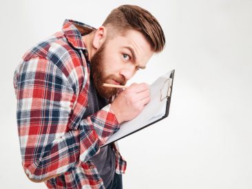 Portrait of a funny bearded man writing notes on clipboard and looking at camera isolated on a white background